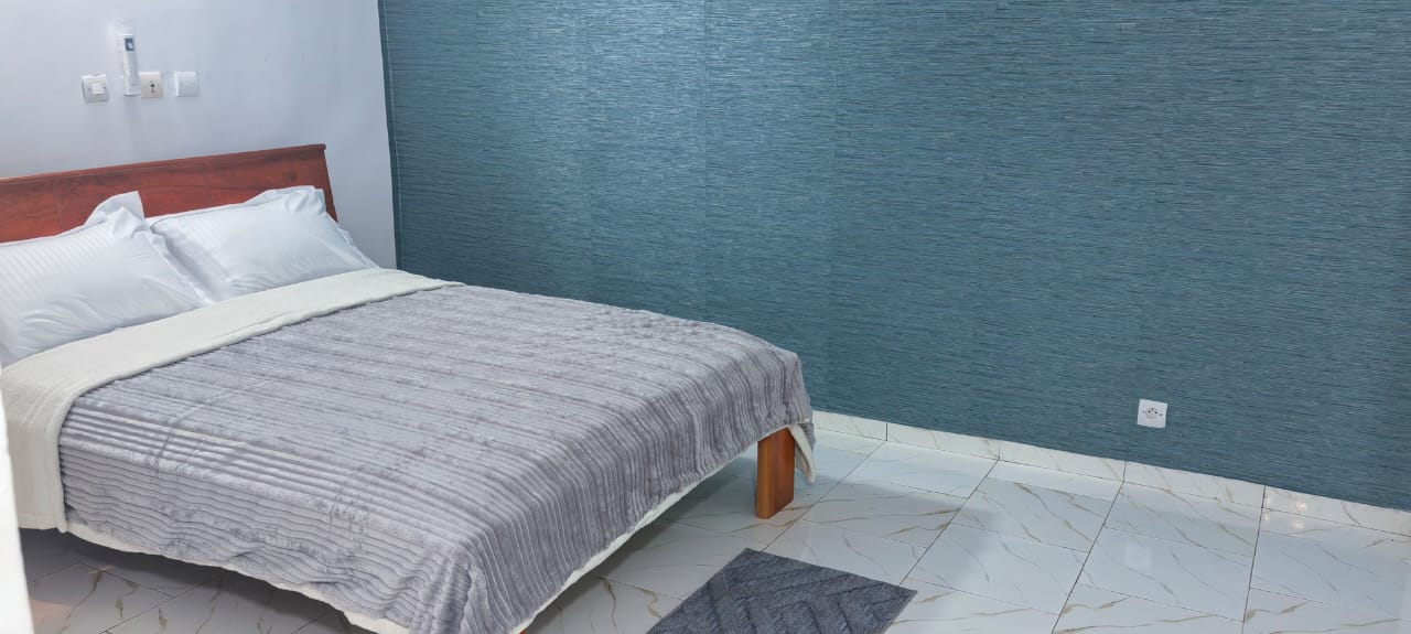 Chambre avec mur bleu teal, lit double et couette grise